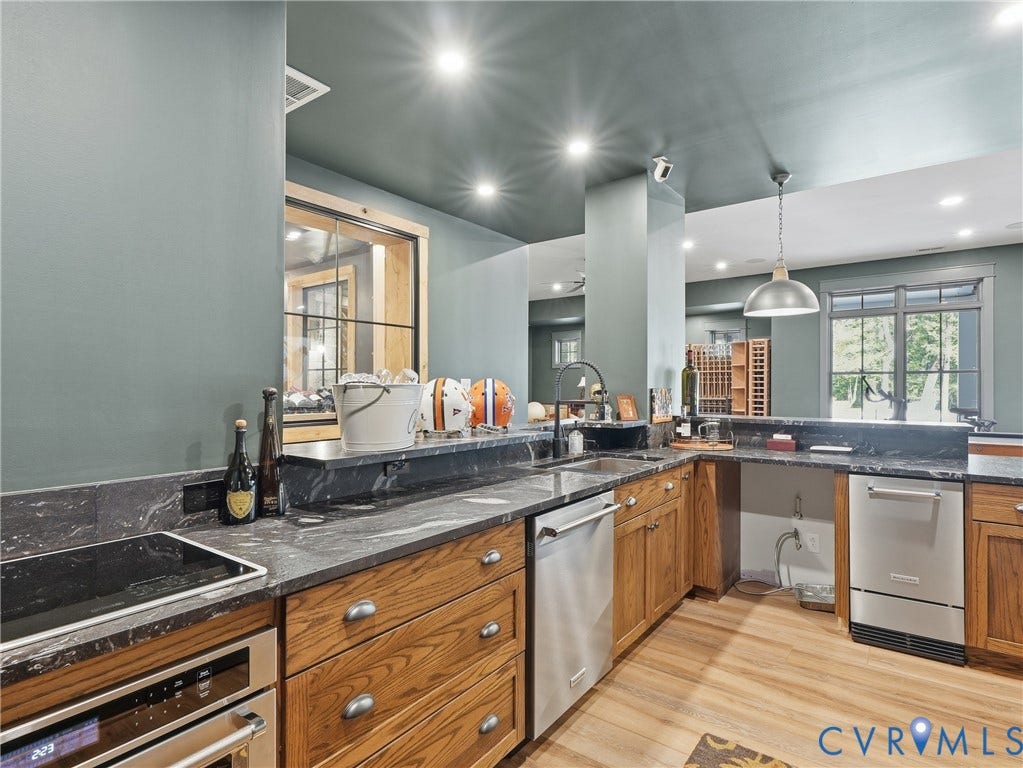 Kitchen featuring wood-finish flooring, custom wood cabinetry, dark stone countertops, and stainless steel appliances