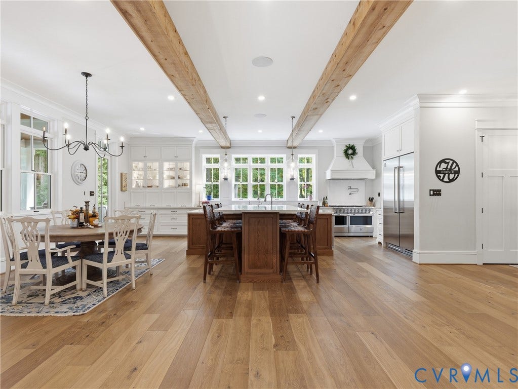 Spacious kitchen with wood-finish flooring, exposed ceiling beams, white cabinetry, a large central island, and stainless steel appliances