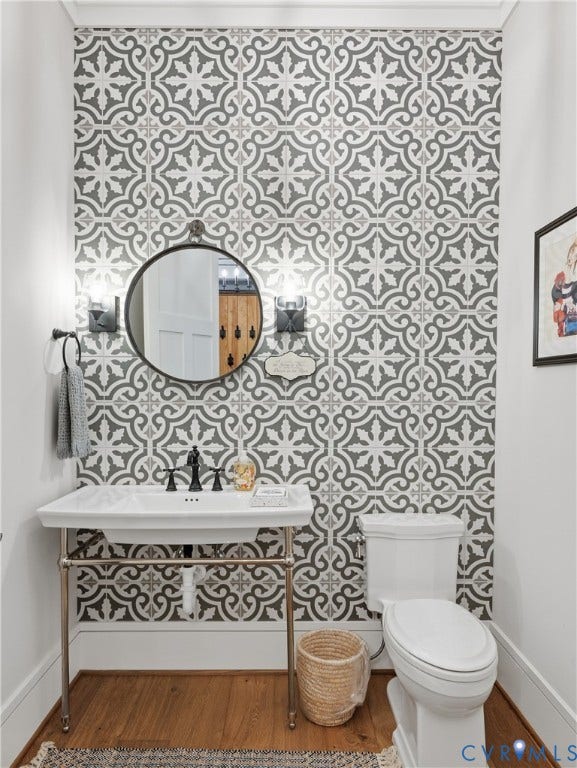Decorative wall tile, pedestal sink with metal base, black faucet, circular mirror, and hardwood flooring
