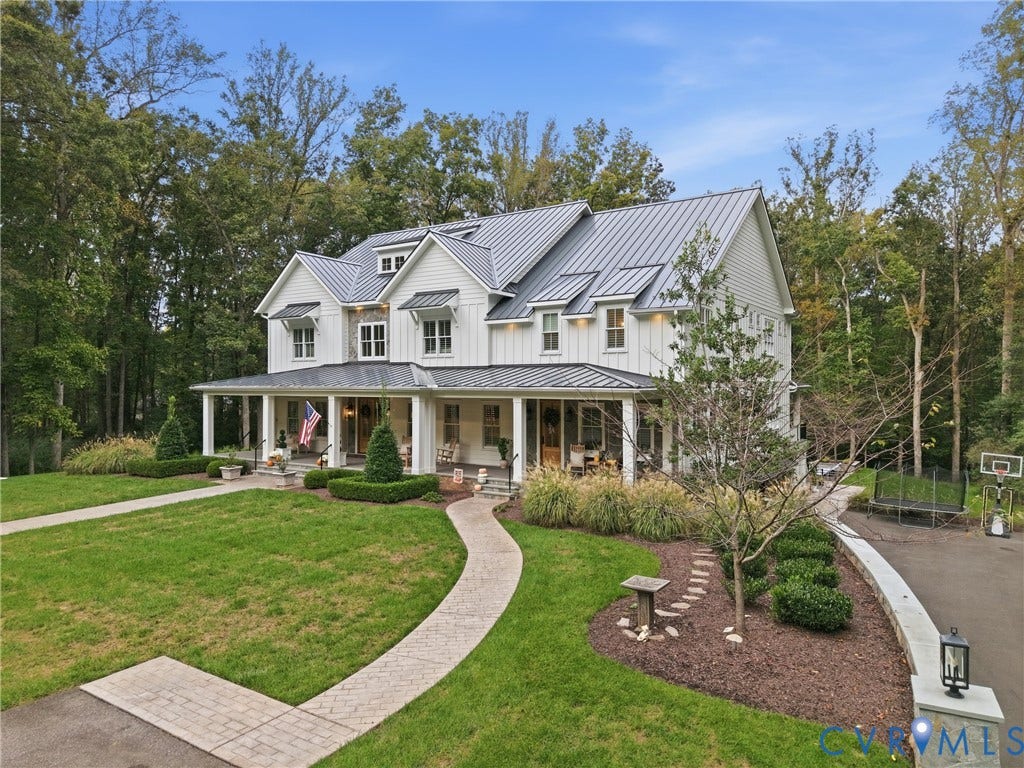 Board and batten siding, metal roof, full-width covered porch, paved driveway, and established landscaping