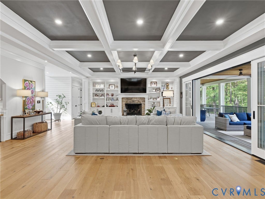 Coffered ceiling with recessed lighting, integrated built-in shelving, stone fireplace, light wood-finish flooring, and expansive sliding glass doors