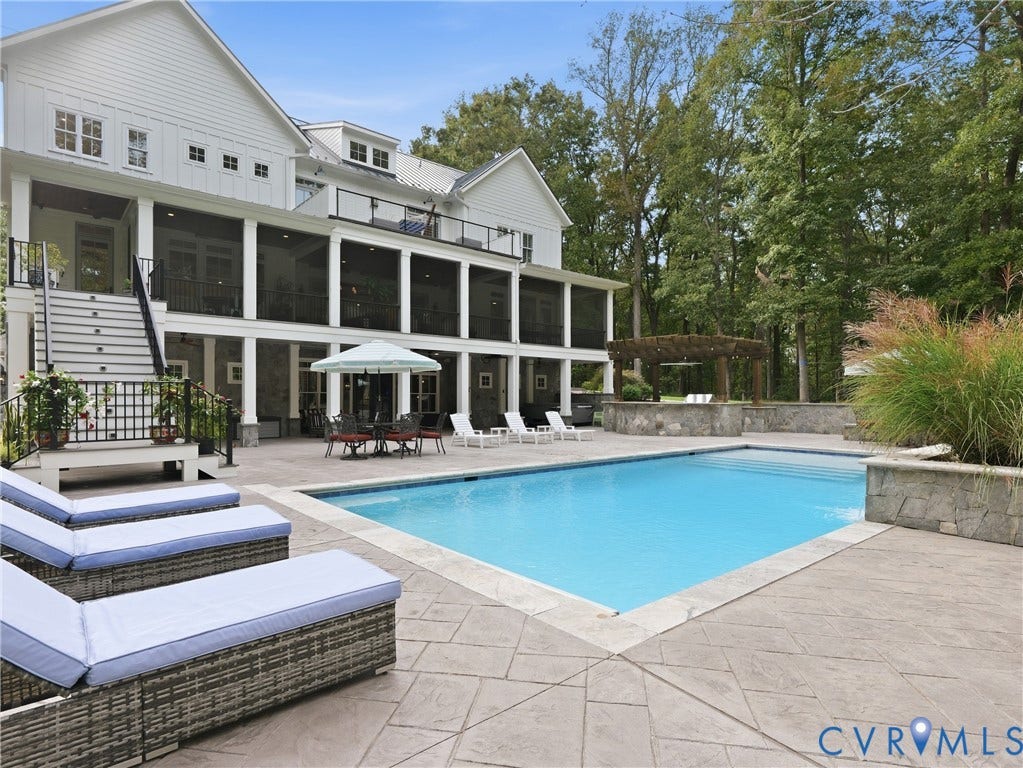 Expansive stamped concrete patio with a rectangular swimming pool, stone accent walls, and a wood pergola