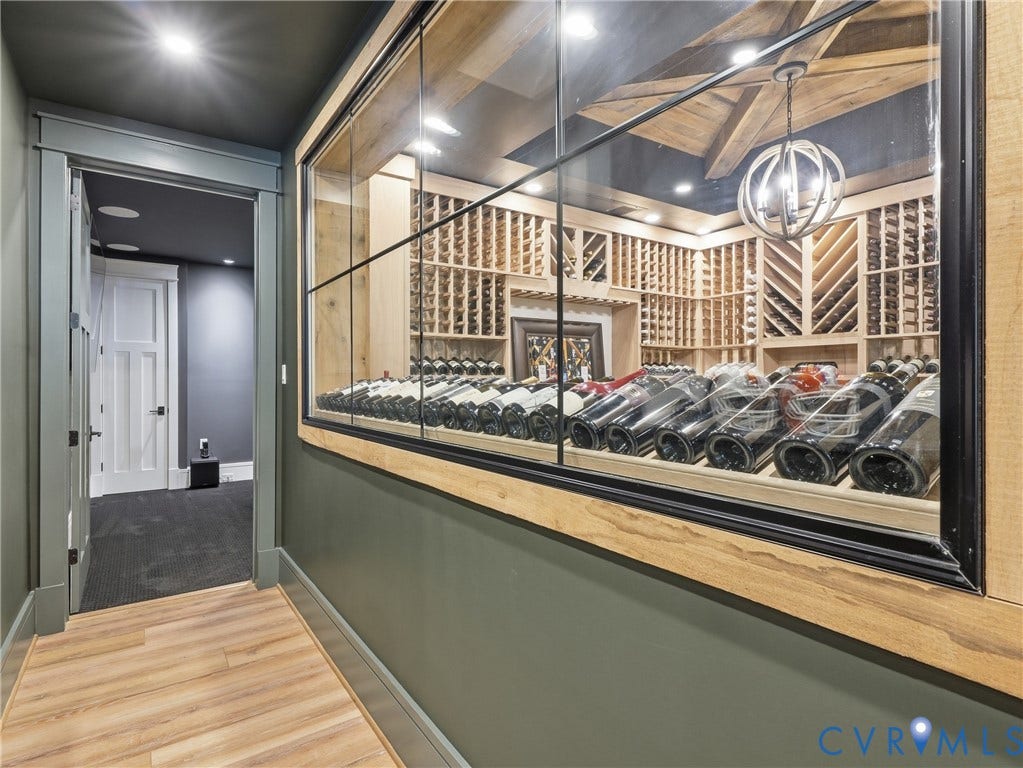 Climate-controlled wine cellar featuring custom wood racking, a glass display wall, exposed ceiling beams, and a modern spherical chandelier