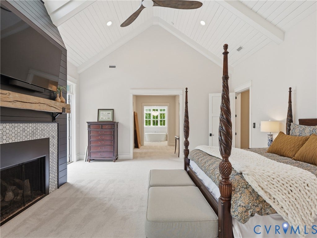 Vaulted ceiling with exposed beams, wood-finish ceiling fan, recessed lighting, fireplace with hex tile surround, and built-in shelving