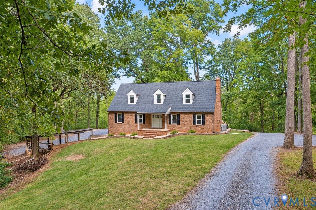 17 River Walk, Cumberland, VA 23027 Brick exterior with dormer windows, a pitched shingle roof, a gravel driveway, and surrounding mature trees
