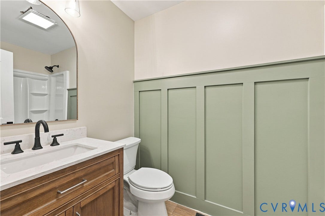 17 River Walk, Cumberland, VA 23027 Bathroom featuring a wood-finish vanity with a white countertop and rectangular sink, matte black faucet, framed mirror, and green board and batten wall treatment