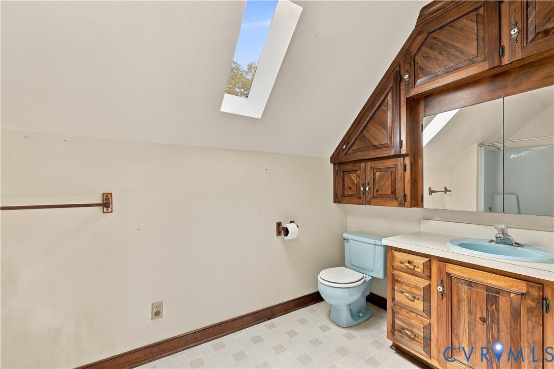 17 River Walk, Cumberland, VA 23027 Slanted ceiling with a skylight, wood-finish cabinetry, vanity with a countertop and integrated sink, and patterned flooring