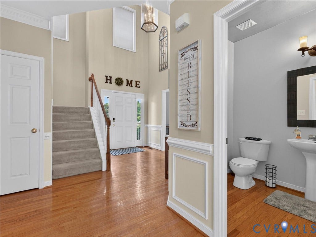 7478 Troub Lane, Elwin Place, Mechanicsville, VA 23111 Double-height entry with wood-finish flooring, a carpeted staircase with wood railing, and a powder room featuring a pedestal sink