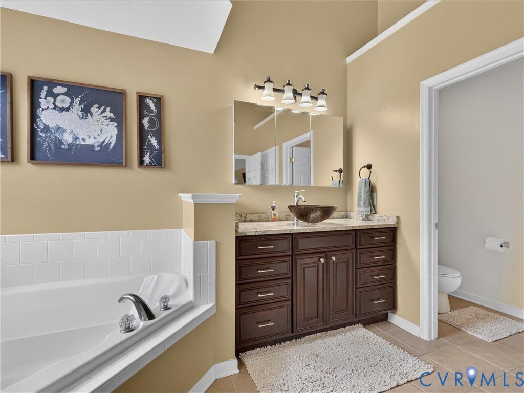 7478 Troub Lane, Elwin Place, Mechanicsville, VA 23111 Built-in soaking tub with tile surround, wood-finish vanity with stone countertop, vessel sink, and wall-mounted light fixture