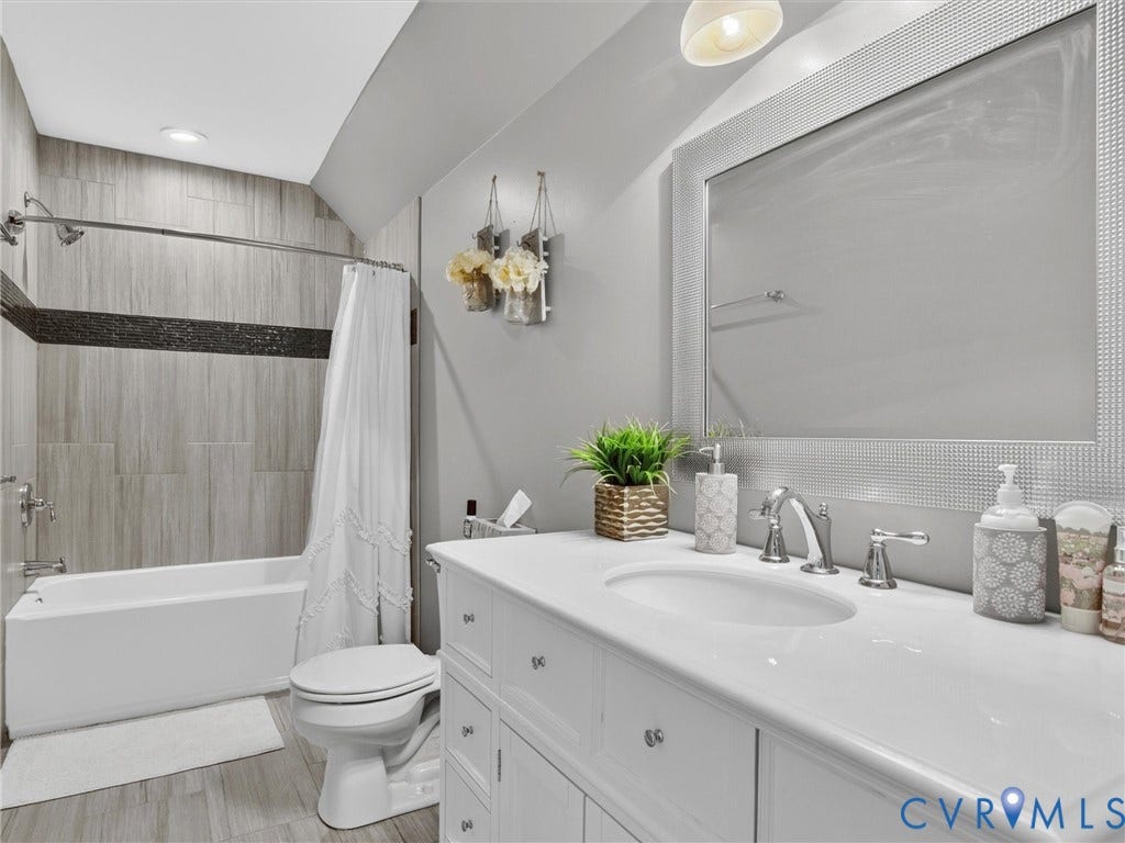 7478 Troub Lane, Elwin Place, Mechanicsville, VA 23111 White vanity with an integrated sink and chrome faucet, large framed mirror, tiled bathtub surround with a dark accent band, and wood-finish flooring