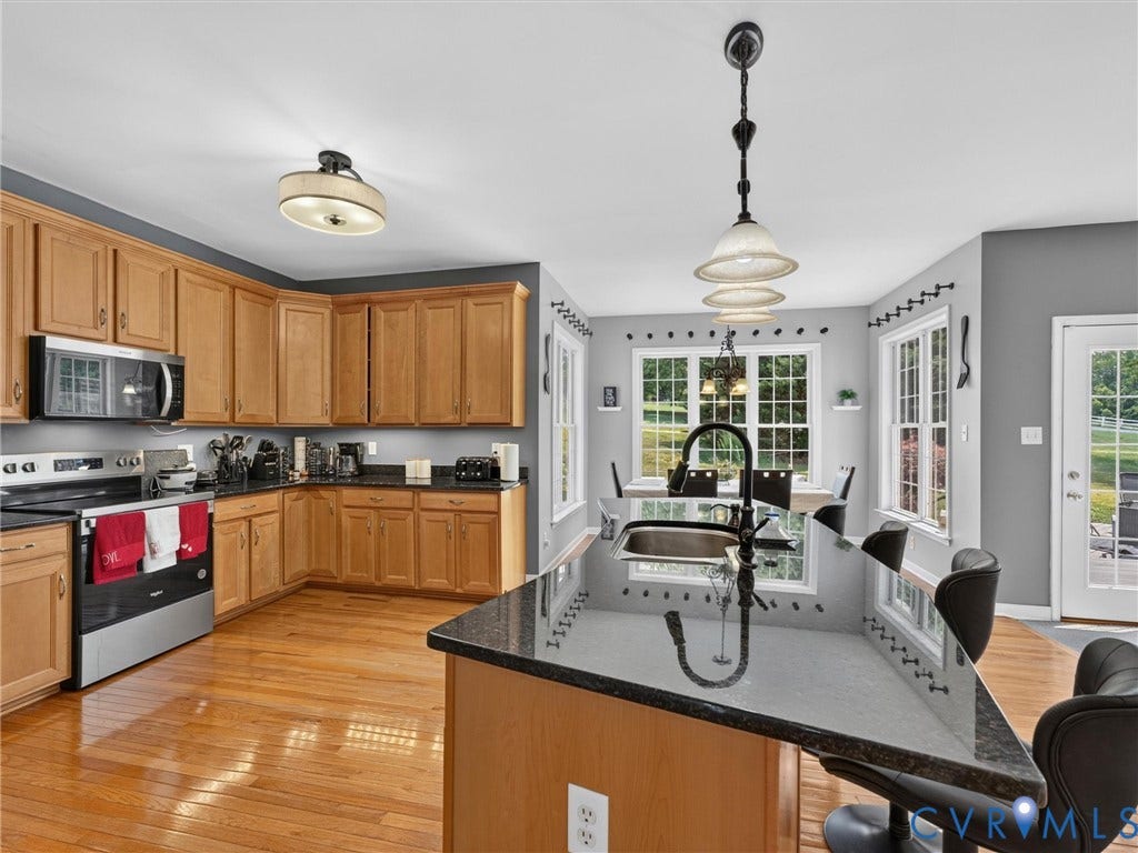 7478 Troub Lane, Elwin Place, Mechanicsville, VA 23111 Hardwood flooring, light wood cabinetry, dark countertops, built-in stainless steel microwave, and a kitchen island with a sink