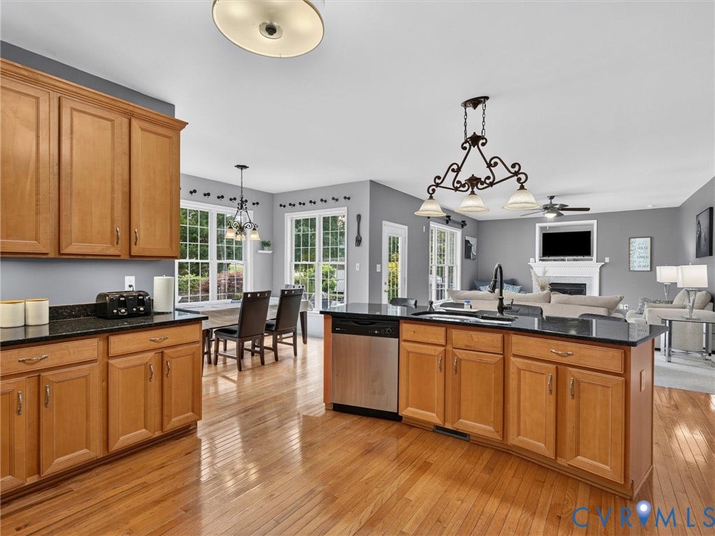 7478 Troub Lane, Elwin Place, Mechanicsville, VA 23111 Open-concept kitchen with wood-finish flooring, light wood cabinetry, black countertops, and a central island with a built-in sink