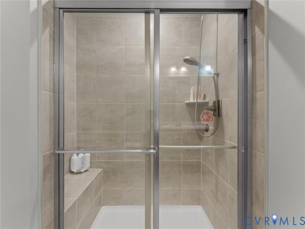 Frameless glass shower enclosure with tiled walls, a built-in shower bench, and a handheld shower fixture