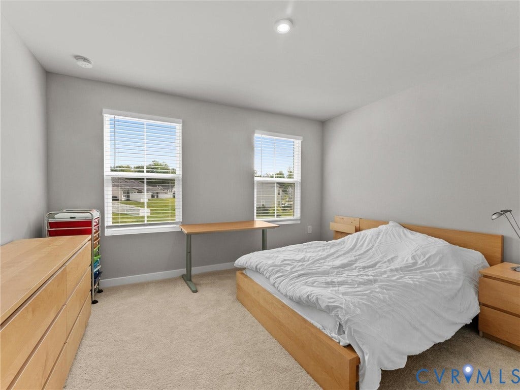 Recessed ceiling lighting, two windows with blinds, light-toned walls, and neutral carpeting