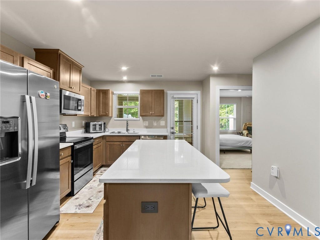 Contemporary kitchen featuring wood-finish flooring, stainless steel appliances, recessed lighting, and a kitchen island with a white countertop