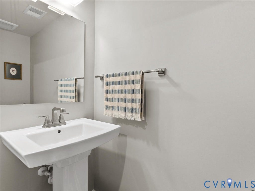 Pedestal sink with a wide basin, brushed nickel faucet, large wall-mounted mirror, and overhead vanity lighting
