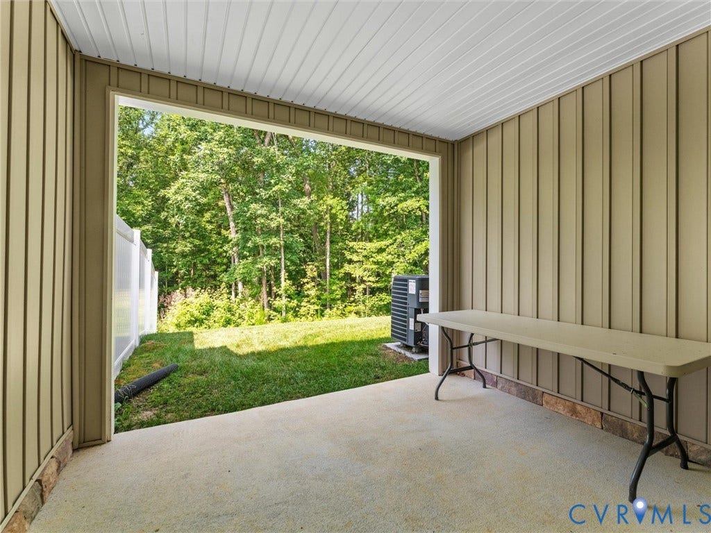 Covered patio with concrete flooring, vertical panel siding, and a translucent panel fence