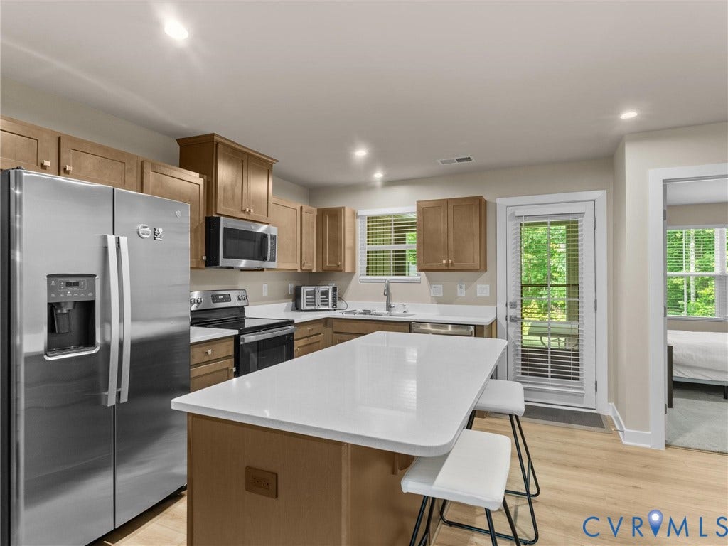 Kitchen featuring stainless steel appliances, wood cabinetry, light countertops, a central island, and wood-finish flooring