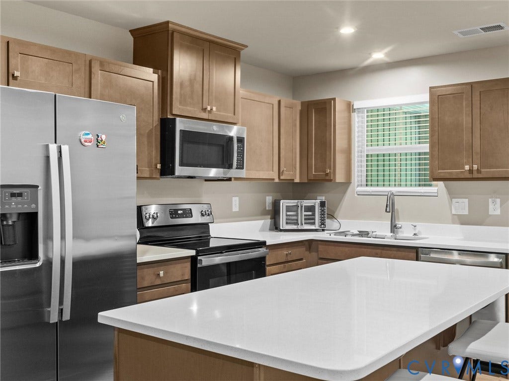Kitchen featuring stainless steel appliances, light wood-finish cabinetry, a white countertop island, and recessed lighting