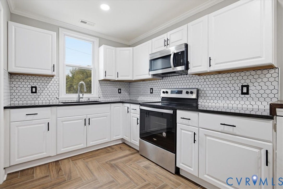 1630 W Washington Street, Petersburg, VA 23803 White cabinetry with black hardware, black countertops, honeycomb tile backsplash, stainless steel appliances, and wood-finish flooring
