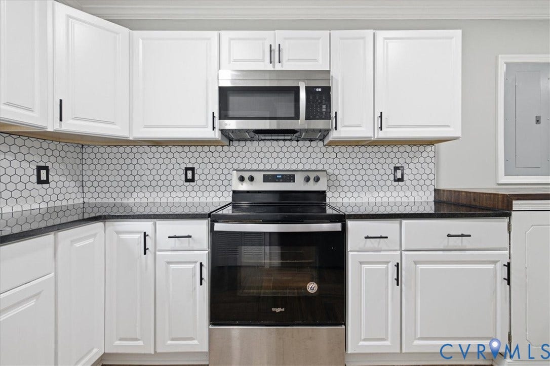 1630 W Washington Street, Petersburg, VA 23803 White shaker-style cabinetry with black hardware, black countertops, hexagonal tile backsplash, stainless steel microwave, and range
