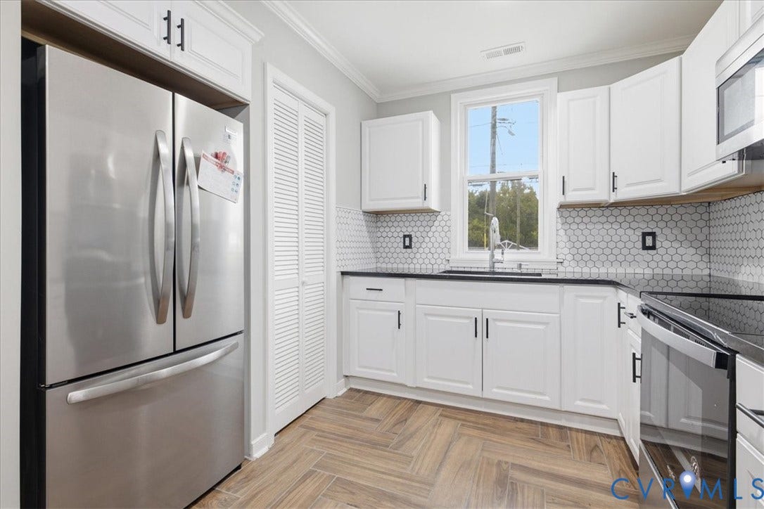 1630 W Washington Street, Petersburg, VA 23803 White shaker cabinetry, black countertops, stainless steel appliances, geometric tile backsplash, and wood-finish flooring