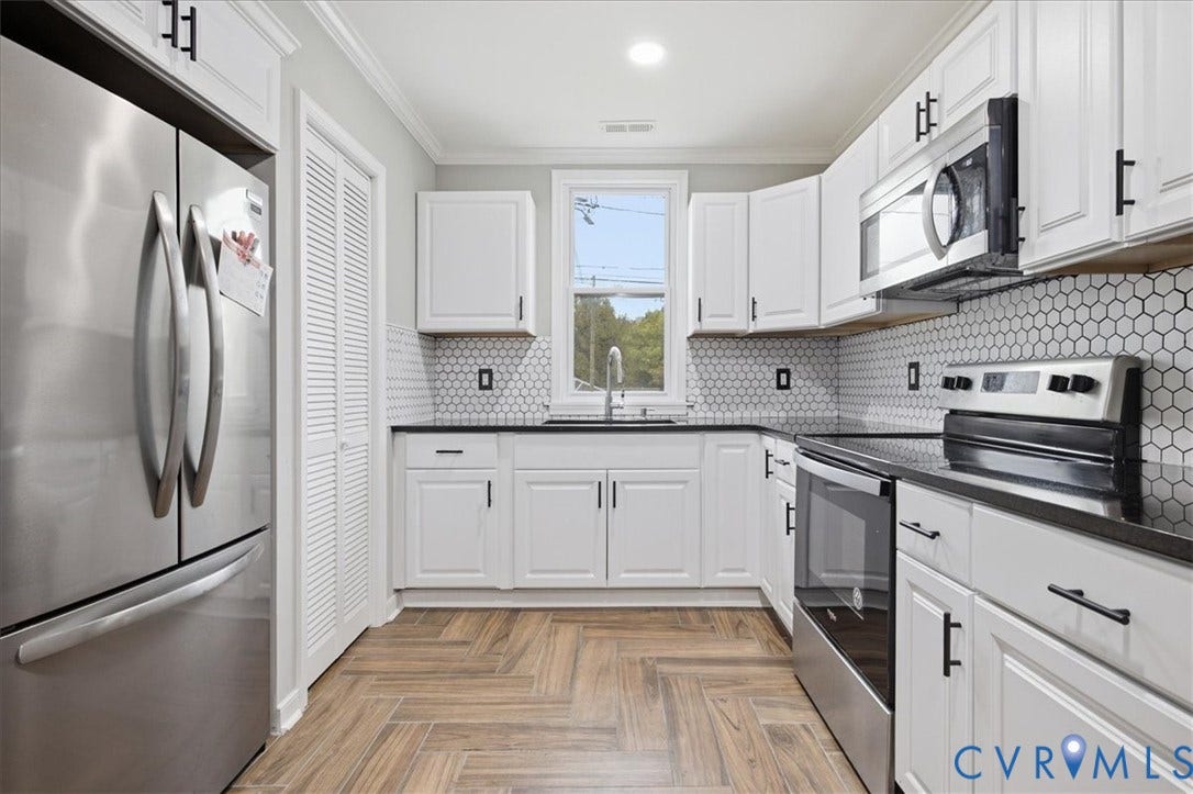 1630 W Washington Street, Petersburg, VA 23803 Kitchen featuring white cabinetry, dark countertops, a hexagonal tile backsplash, stainless steel appliances, and herringbone-patterned wood-finish flooring