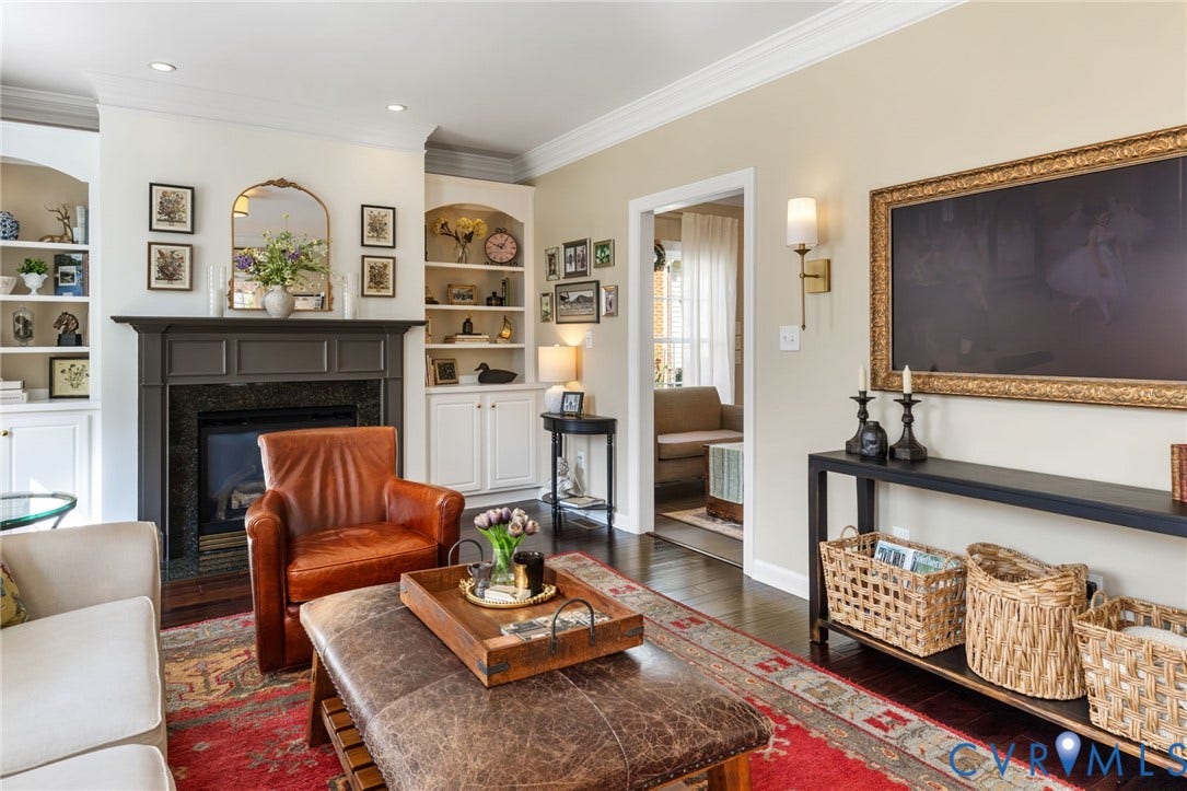 Hardwood flooring, crown molding, built-in shelving, fireplace with dark mantel, and wall sconce lighting