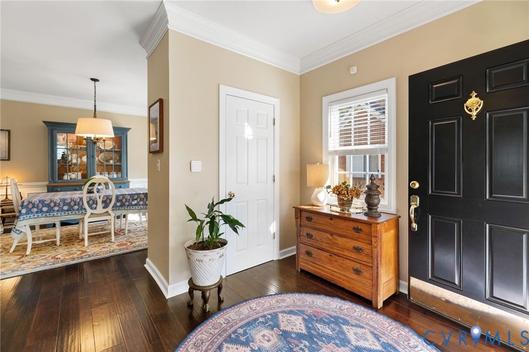 Rich wood-finish flooring, crown molding, and a paneled entry door with brass hardware
