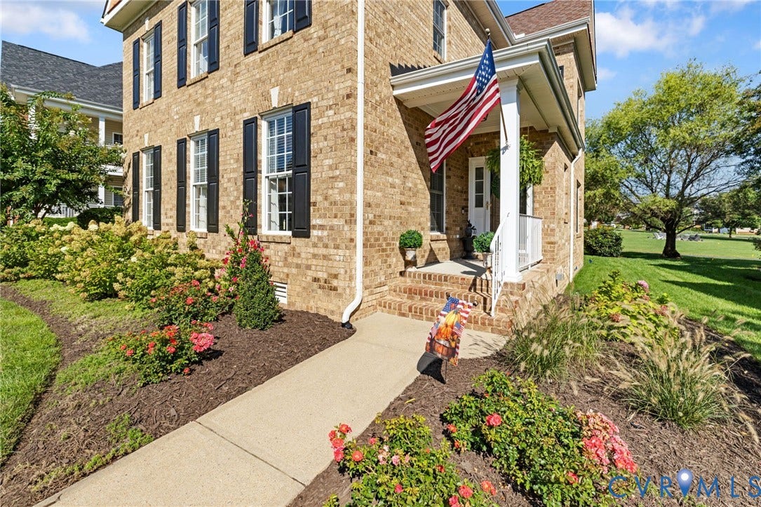 Brick exterior featuring a covered front porch, white railings, and dark louvered shutters