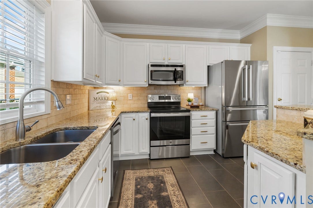 White cabinetry, stainless steel appliances, dual basin sink, light-toned backsplash tiling, and stone countertops