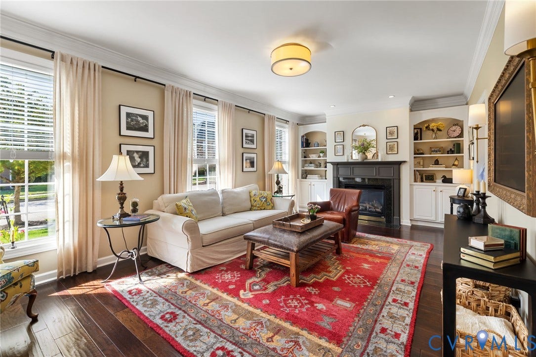 Living area featuring rich wood-finish flooring, multiple windows with blinds, a fireplace with a dark mantel, and built-in shelving with lower cabinetry