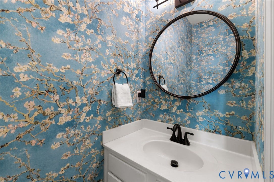 Wall-mounted circular mirror, vanity with integrated sink, matte black faucet, and patterned wallpaper