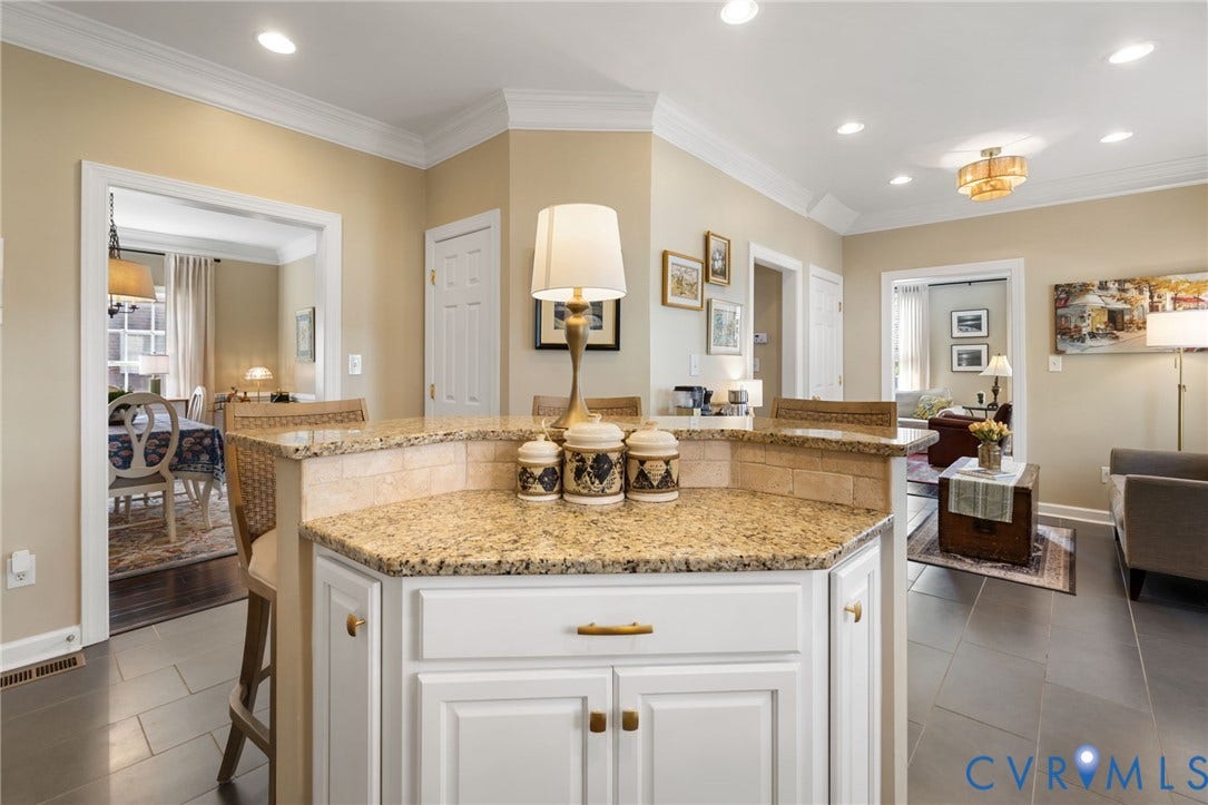 Kitchen island with a granite countertop, white cabinetry, brass hardware, and a tile backsplash