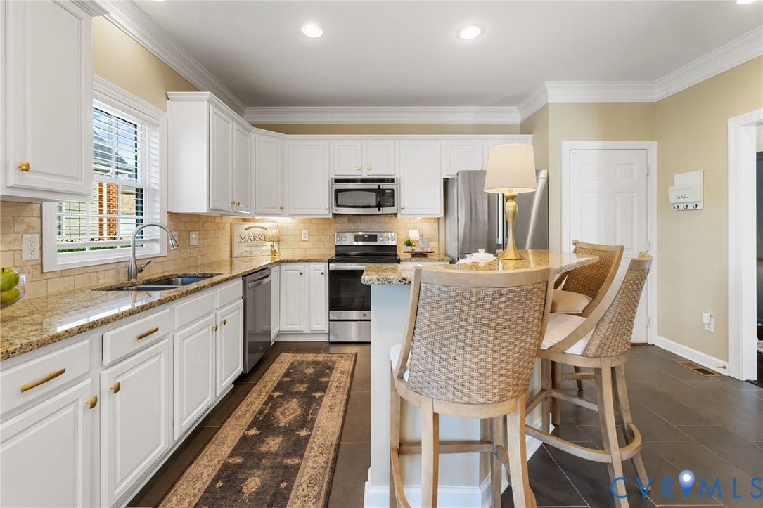 White cabinetry with gold-tone hardware, granite countertops, stainless steel appliances, tile backsplash, and dark tile flooring