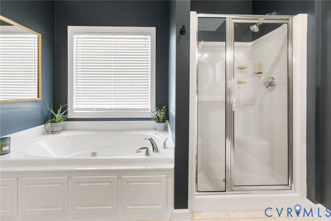 Soaking tub with white paneling, chrome fixtures, and an integrated window with blinds