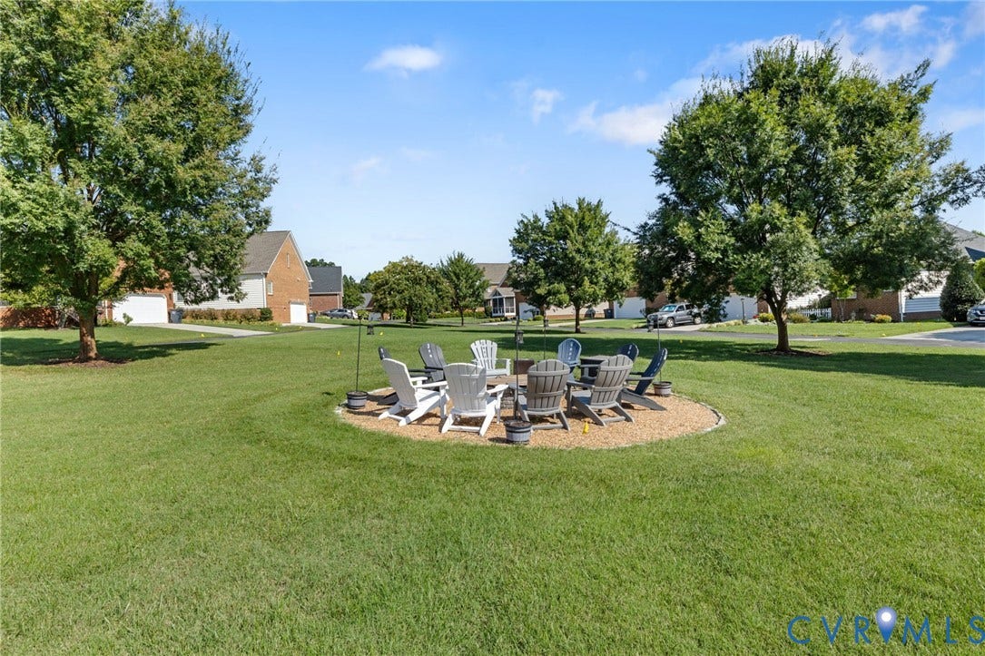 Expansive green lawn with mature shade trees and a landscaped fire pit area