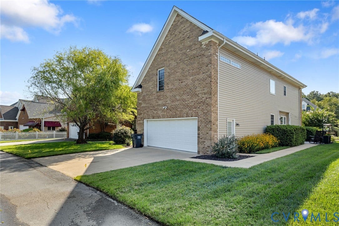 Brick and siding exterior with an attached garage, paved driveway, and established landscaping
