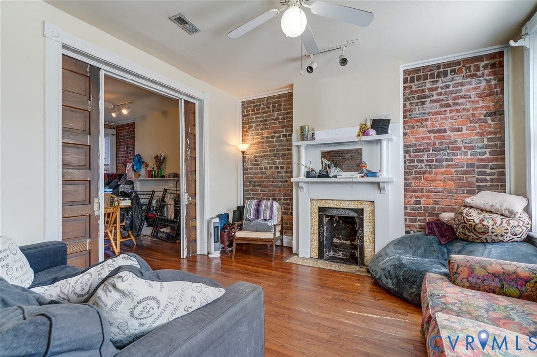 1620 W Cary Street, Fan Extenstion, Richmond, VA 23220 Exposed brick accent walls, wood-finish flooring, a decorative fireplace with a white mantel, and ceiling-mounted track lighting