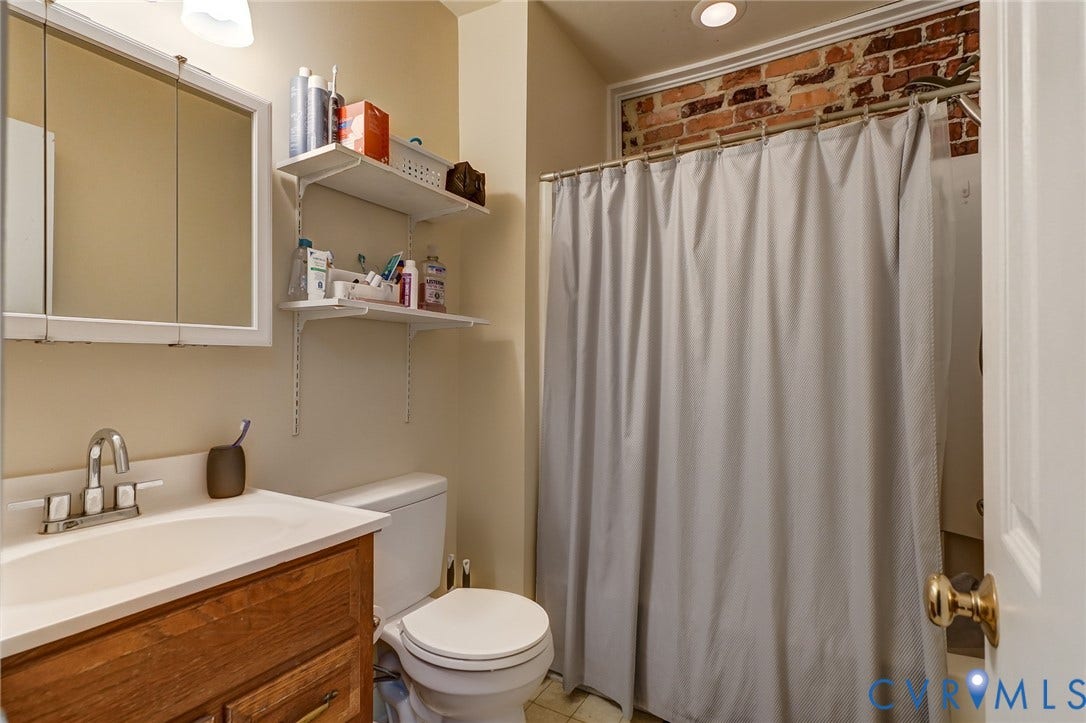 1620 W Cary Street, Fan Extenstion, Richmond, VA 23220 Wood-finish vanity with an integrated sink, polished chrome faucet, white medicine cabinet, and exposed brick accent wall