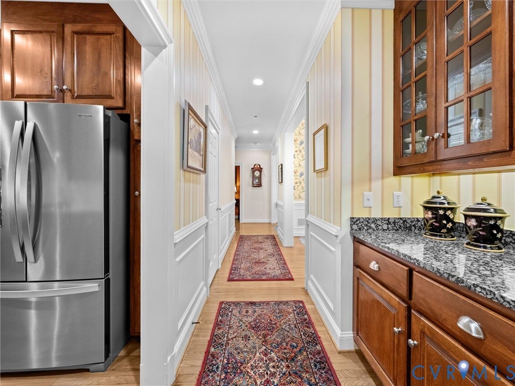 Stainless steel refrigerator, wood-finish cabinetry, stone countertop, glass-front upper cabinets, and beadboard wall paneling