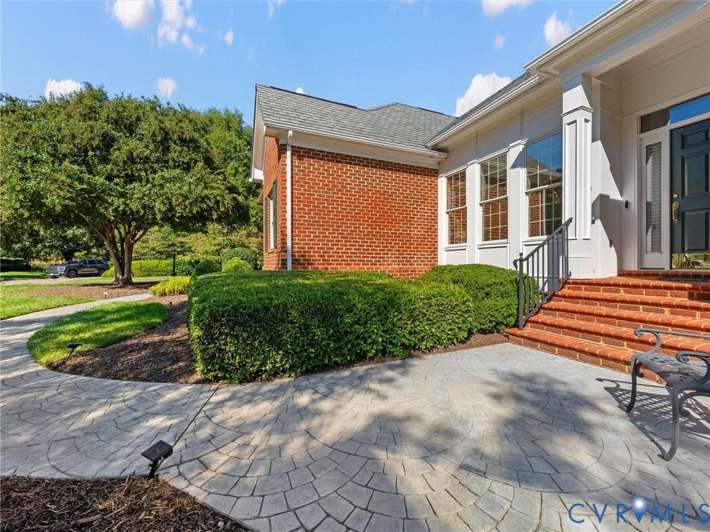 Brick and white siding exterior with a dark entry door, brick steps with a black metal handrail, and an imprinted concrete pathway