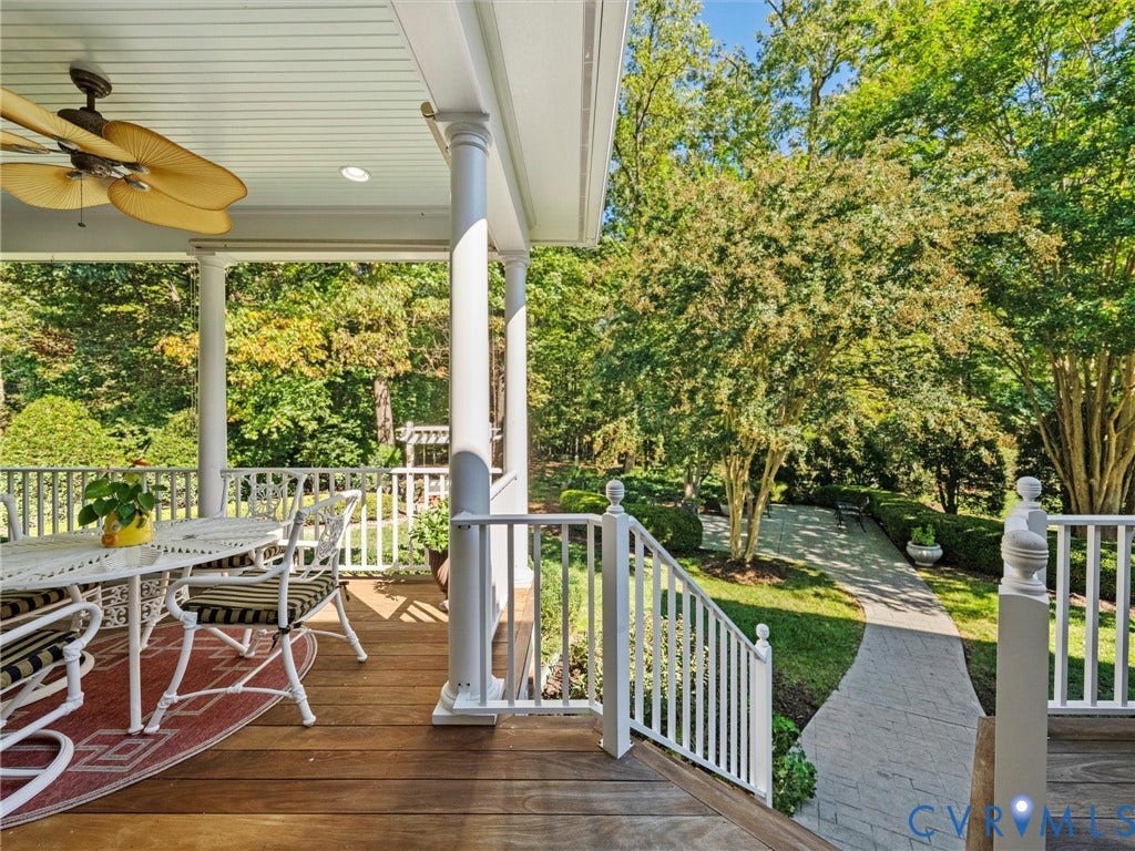 Covered porch featuring wood-finish flooring, white railing, decorative columns, and a ceiling fan