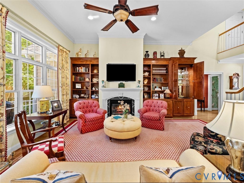 Vaulted ceiling with a ceiling fan, a fireplace with a white mantel, built-in wooden bookshelves, hardwood flooring, and large windows