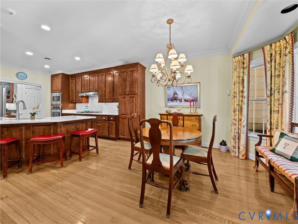 Kitchen and dining area featuring wood-finish flooring, custom wood cabinetry, stainless steel appliances, and a white countertop island with an integrated sink