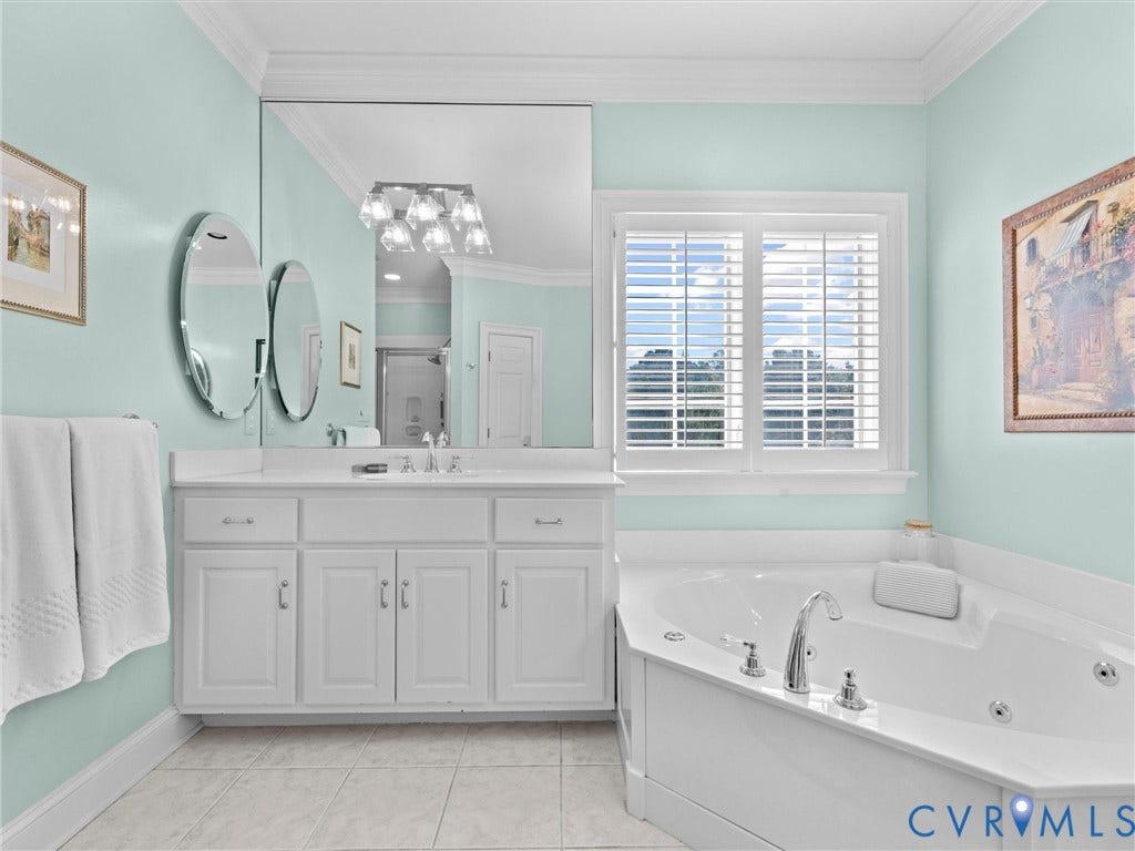 White cabinetry with brushed nickel hardware, expansive mirrored wall, white plantation shutters, and a built-in corner jetted tub with chrome fixtures