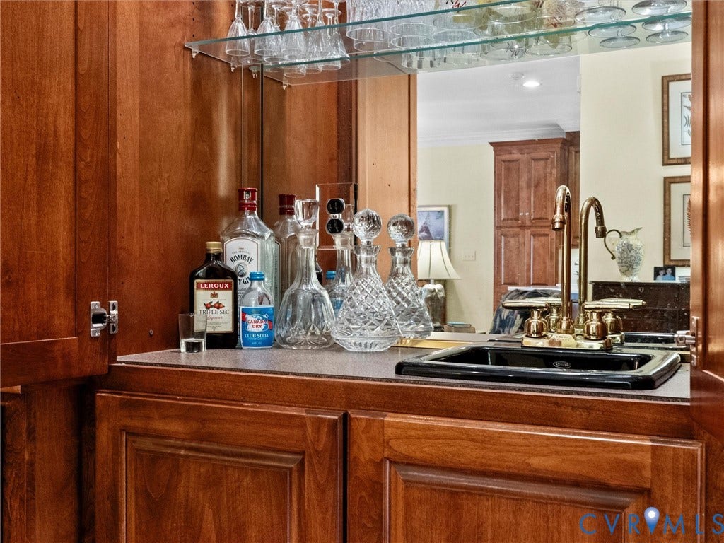 Built-in wet bar featuring custom wood cabinetry, a polished brass faucet, an under-mount sink, and integrated glass shelving