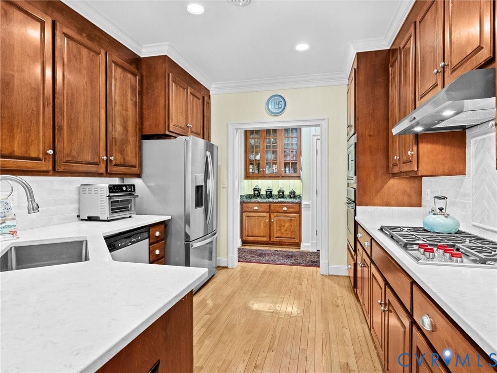 Well-appointed kitchen featuring wood cabinetry, stainless steel appliances, light-toned countertops, and hardwood flooring