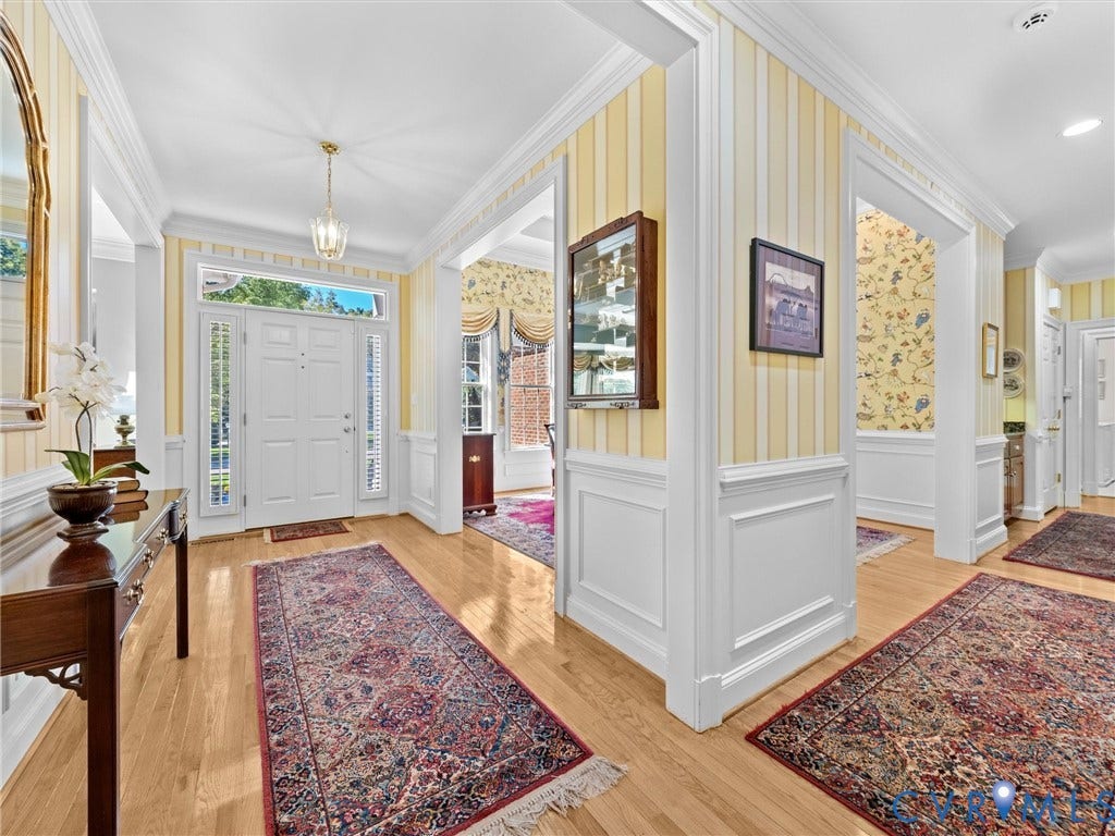 Hardwood flooring, white paneled entry door with sidelights and transom, recessed lighting, decorative crown molding, and wainscoting