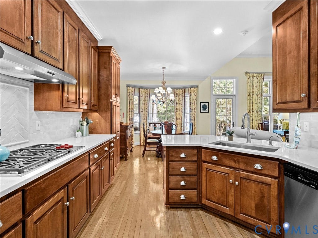 Kitchen featuring wood cabinetry, light-toned countertops, a stainless steel range hood, stainless steel sink, and wood-finish flooring